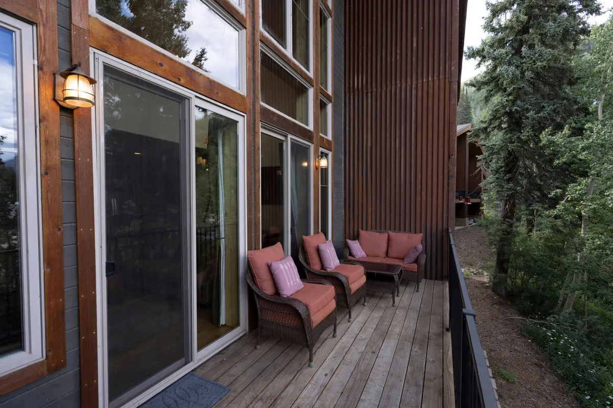 A tranquil outdoor seating area framed by large windows and surrounded by natural scenery. Comfortable chairs invite relaxation or socializing, with easy access to both the home and the outdoors.