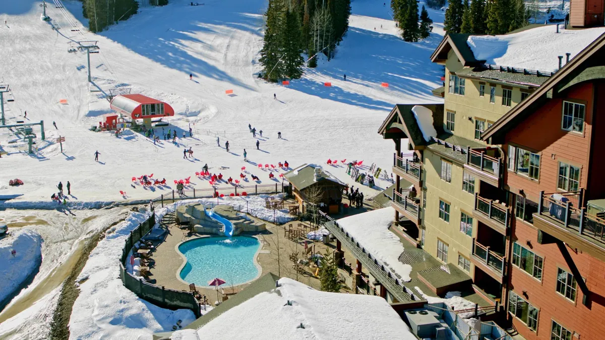 This vibrant exterior image captures the ski slopes directly adjacent to a lodge, with a swimming pool, ski lift, and families enjoying the snow. It provides a clear view of the ski-in/ski-out access as well as the lively atmosphere around the slopes, perfectly echoing the excitement of family-friendly mountain adventures.