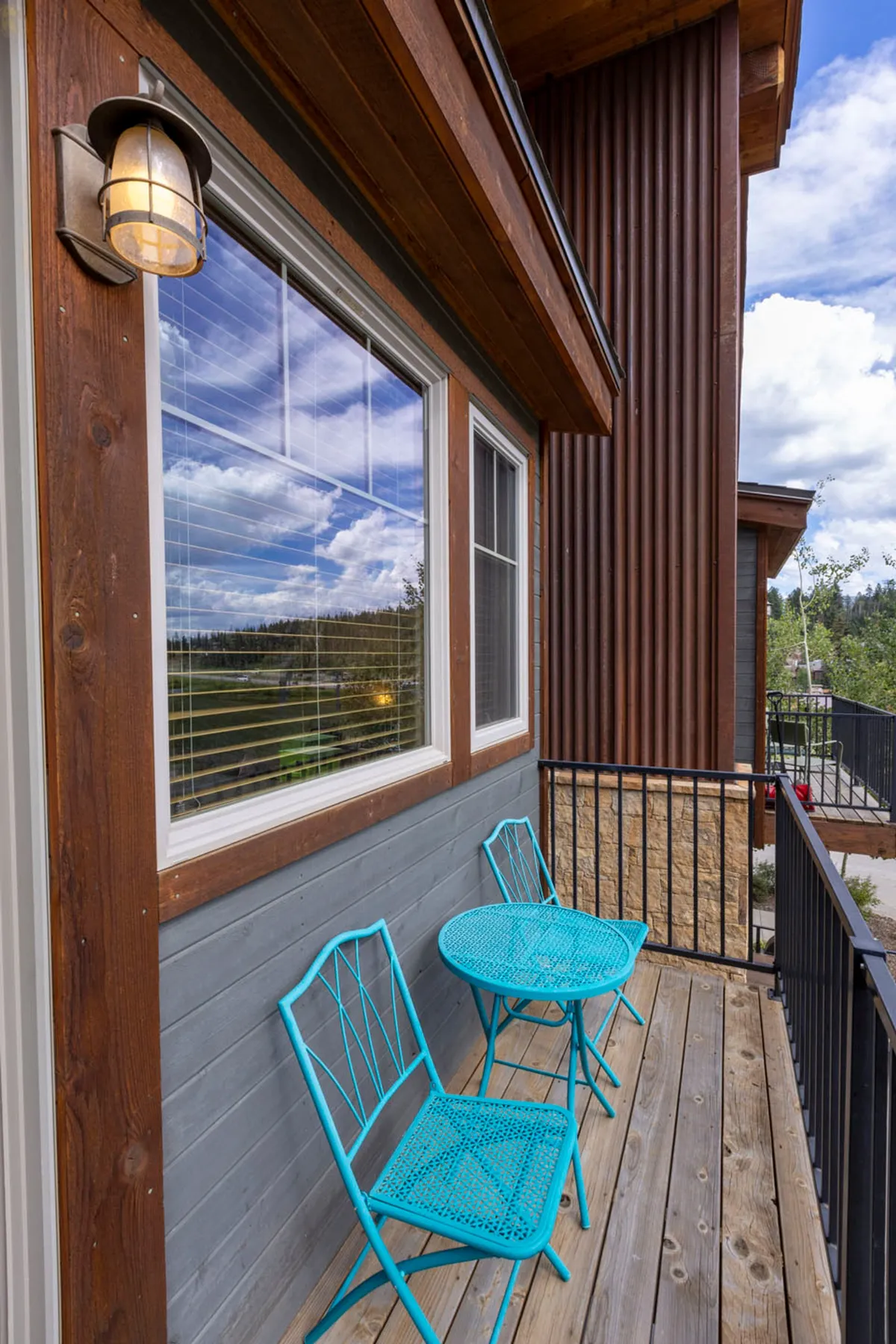 A wooden deck with blue metal chairs and a small round table, offering a relaxed spot for morning coffee or evening stargazing. The deck overlooks beautiful mountain scenery, with reflections in the nearby window enhancing the sense of openness to nature.