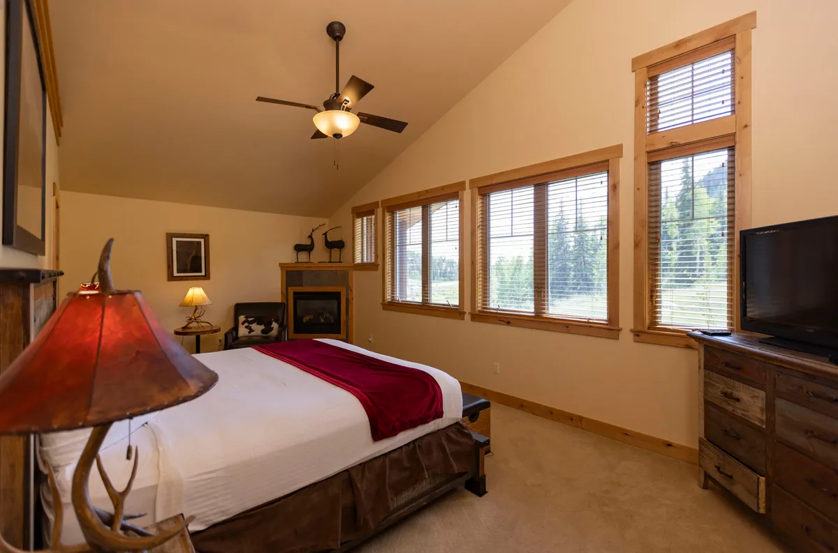 A serene bedroom with a bed adorned with a red throw, large windows, and a fireplace. The view from the bed looks out on the landscape, and the warm glow of the fire creates a peaceful retreat for post-adventure relaxation.
