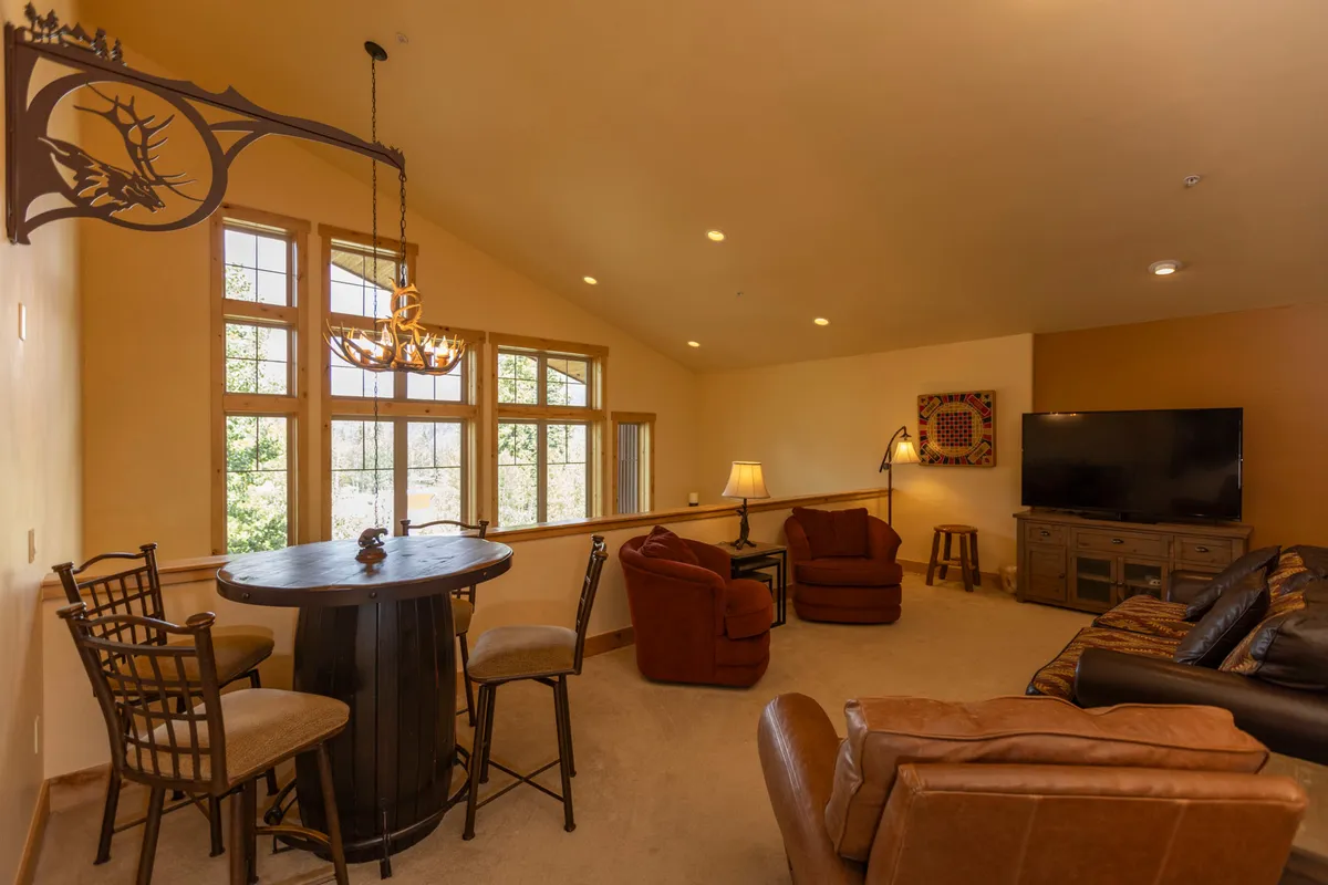 This interior features a cozy seating area with a bar table and stools, large windows framing scenic views, and a television unit. The setup is ideal for socializing, watching TV, or relaxing with a book, aligning with the idea of a flexible family space. The natural light and casual arrangement add to the welcoming, adaptable feel.