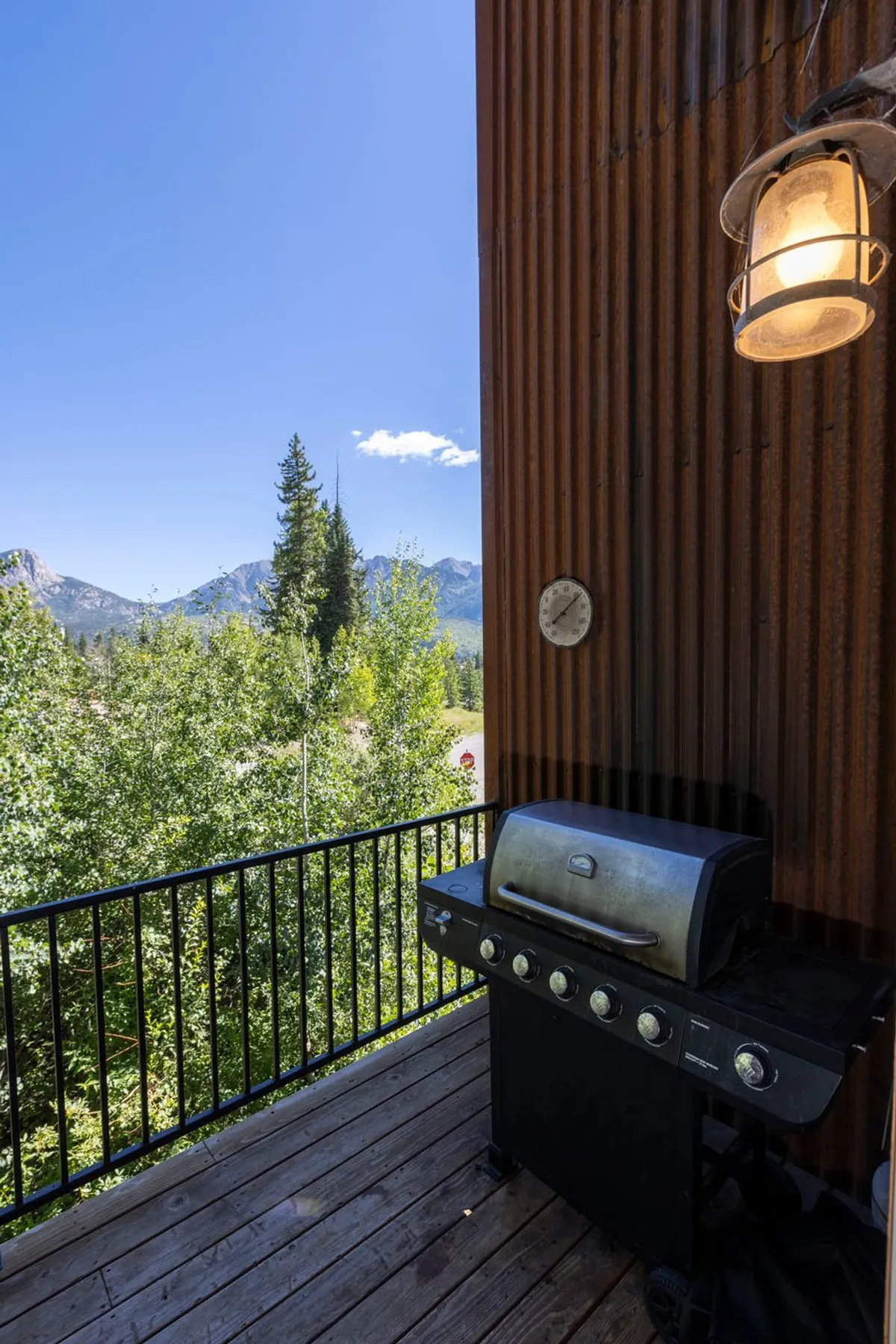 This image features a spacious wooden deck equipped with a barbecue grill and rustic wall, overlooking a stunning mountain view. The deck offers a perfect spot for group gatherings, outdoor dining, and relaxation amid natural surroundings.