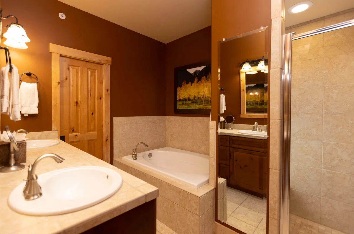 This spa-inspired bathroom is equipped with a relaxing bathtub, double sinks with granite countertops, wooden cabinetry, and framed artwork. The atmosphere is serene and perfect for unwinding after a day of mountain adventures.