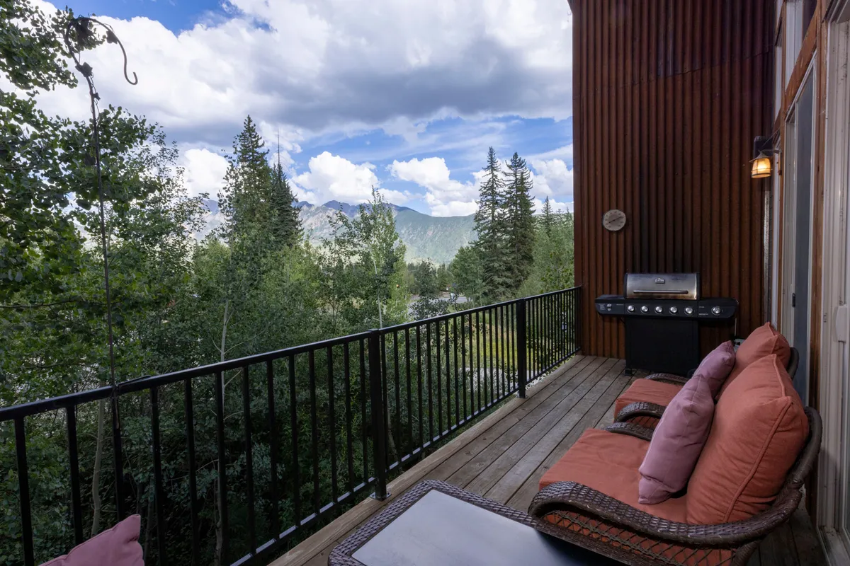 A cozy outdoor seating area on a deck with a backdrop of vast mountain views and a grill. The scene conveys relaxation after an active day, with space for families to gather and take in the surrounding beauty.