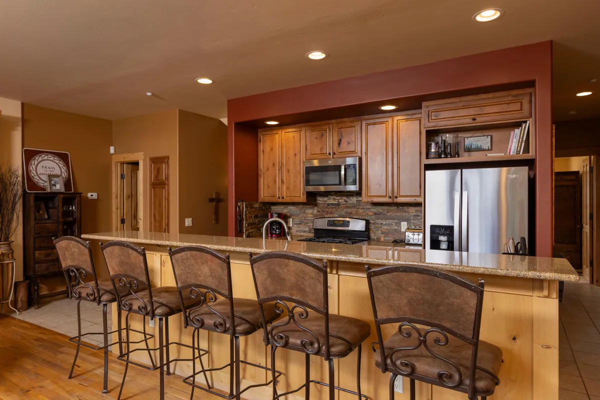 A cozy, well-equipped kitchen with granite countertops, wooden cabinetry, modern appliances, and bar stools for casual seating. The space is designed for cooking and entertaining, with plenty of room for shared meal preparation and conversation.