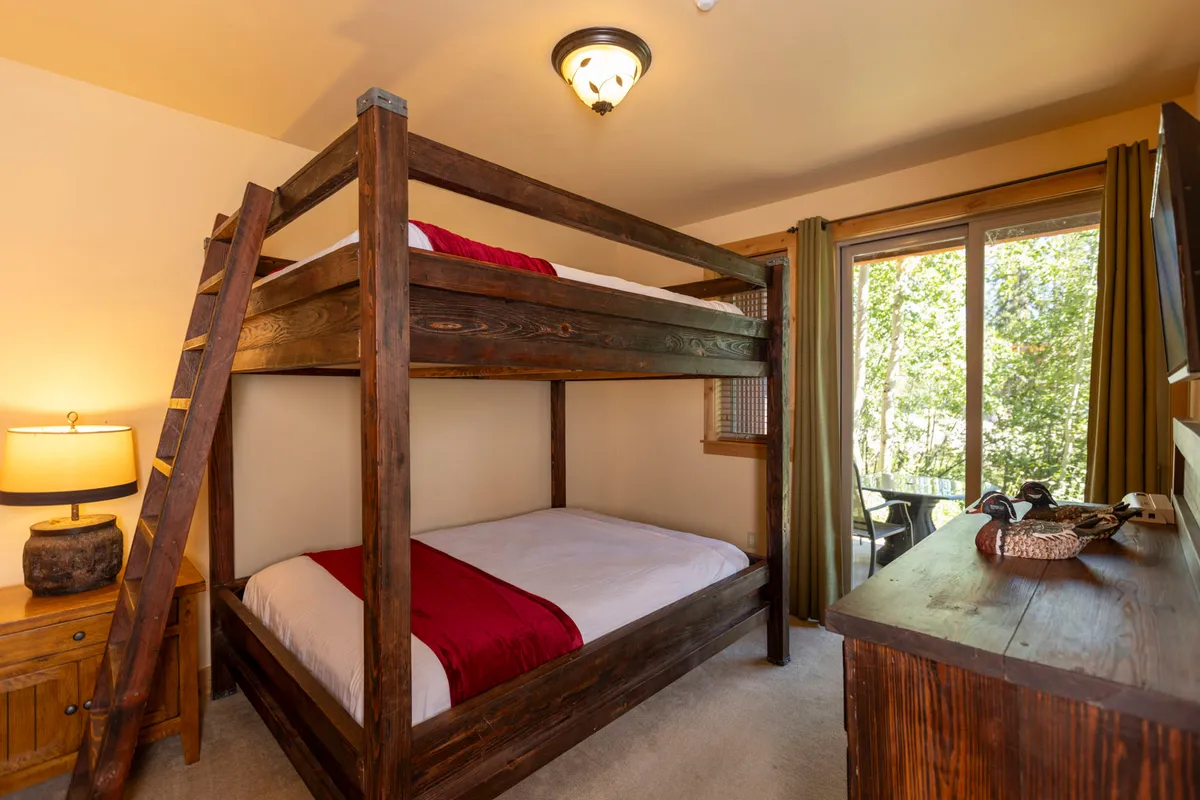 A playful and family-friendly bedroom featuring a sturdy bunk bed, a convenient nightstand with lamp, and expansive windows that let in natural light. The decor is simple yet welcoming, making it an ideal space for children or teens to unwind.