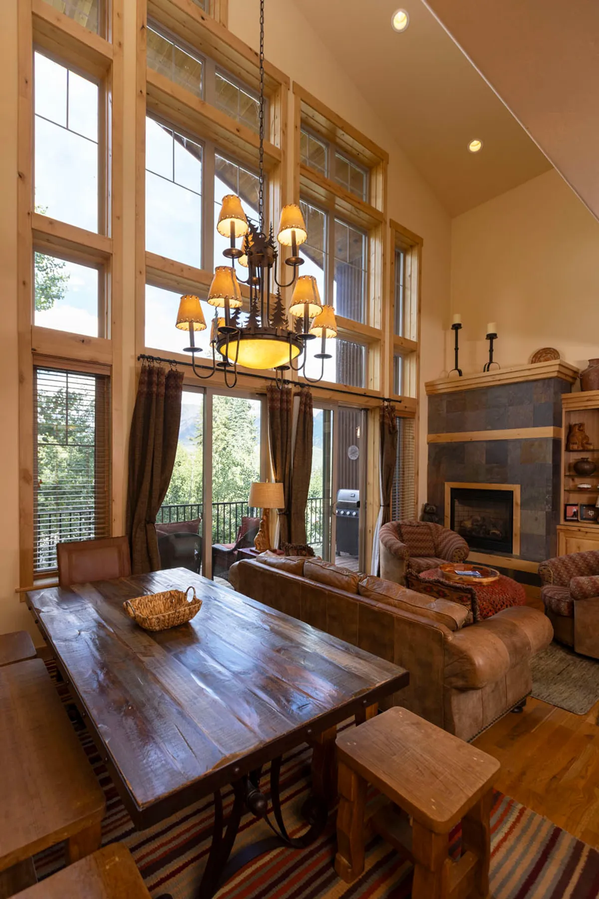 A spacious, cozy interior living and dining area with large windows offering scenic sunrise views. The room features comfortable seating, a wooden dining table, and a chandelier, creating a warm and welcoming ambiance ideal for gathering after a day outdoors.