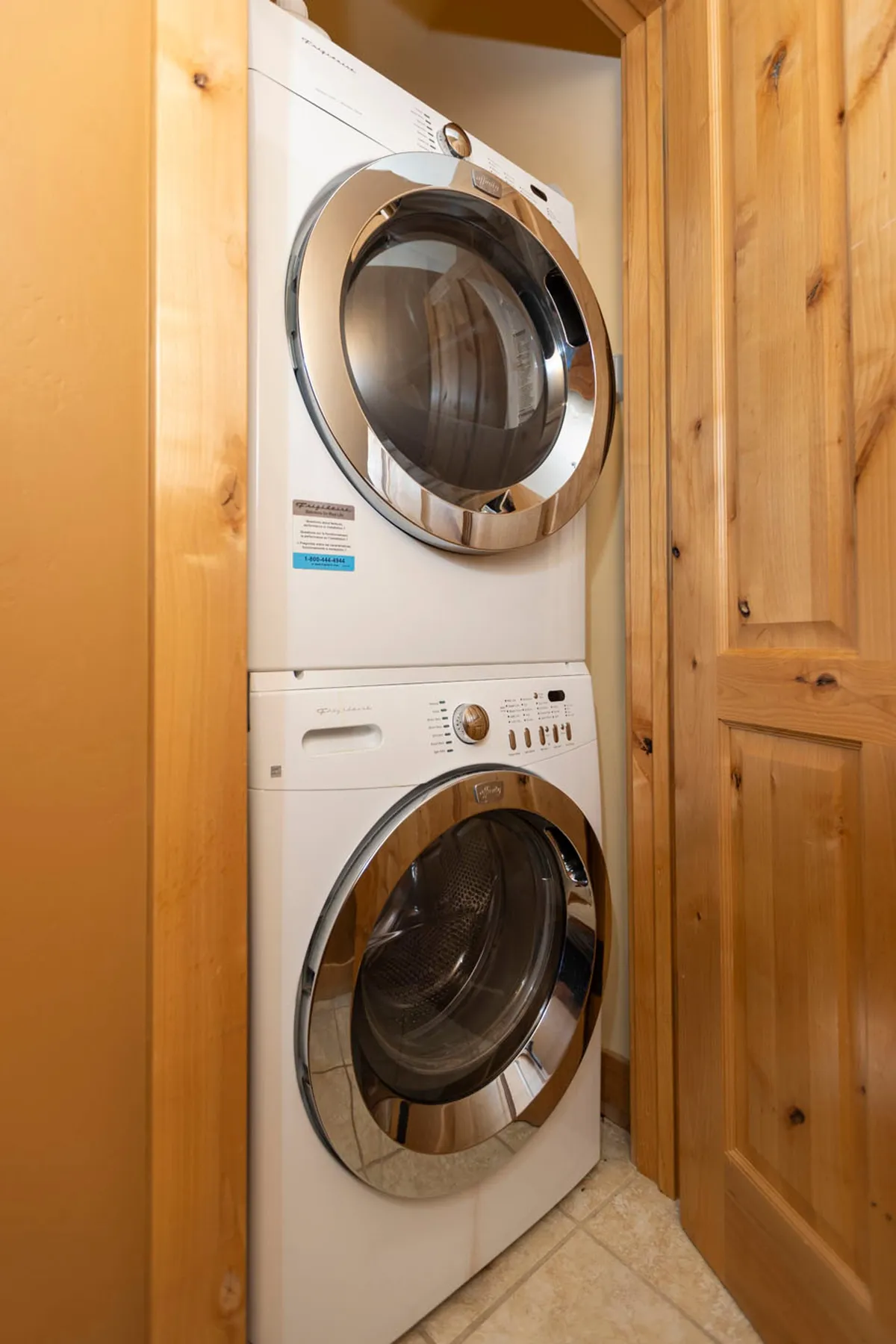 This image features a stacked washer and dryer unit set beside a wooden door, capturing a practical corner likely within a dedicated laundry or mudroom space. The focus is on the convenience and organization essential for managing ski gear and apparel.