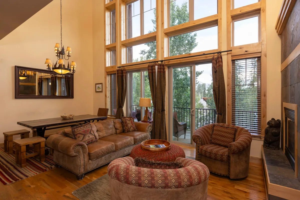 A welcoming interior space with large windows, comfortable seating, a fireplace, and a decorative chandelier. The scene exudes coziness and serves as a transition area where guests can unwind after outdoor activities, likely adjacent to the entry or central living zone.